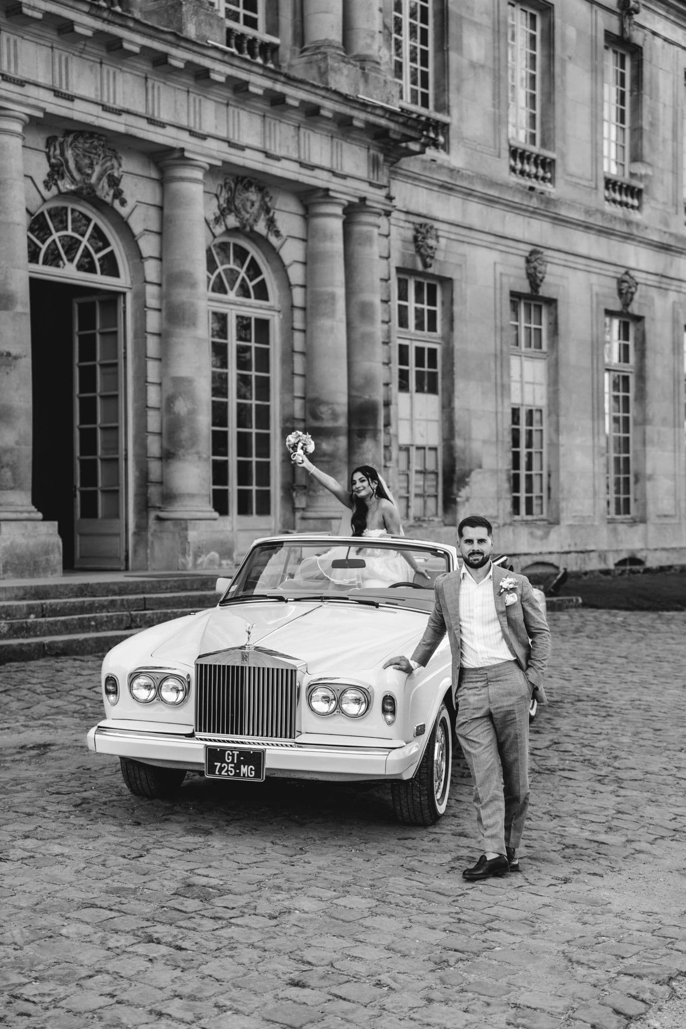 mariés marine et maxime posant sur la rolls royce portrait en noir et blanc au château de champlatreux