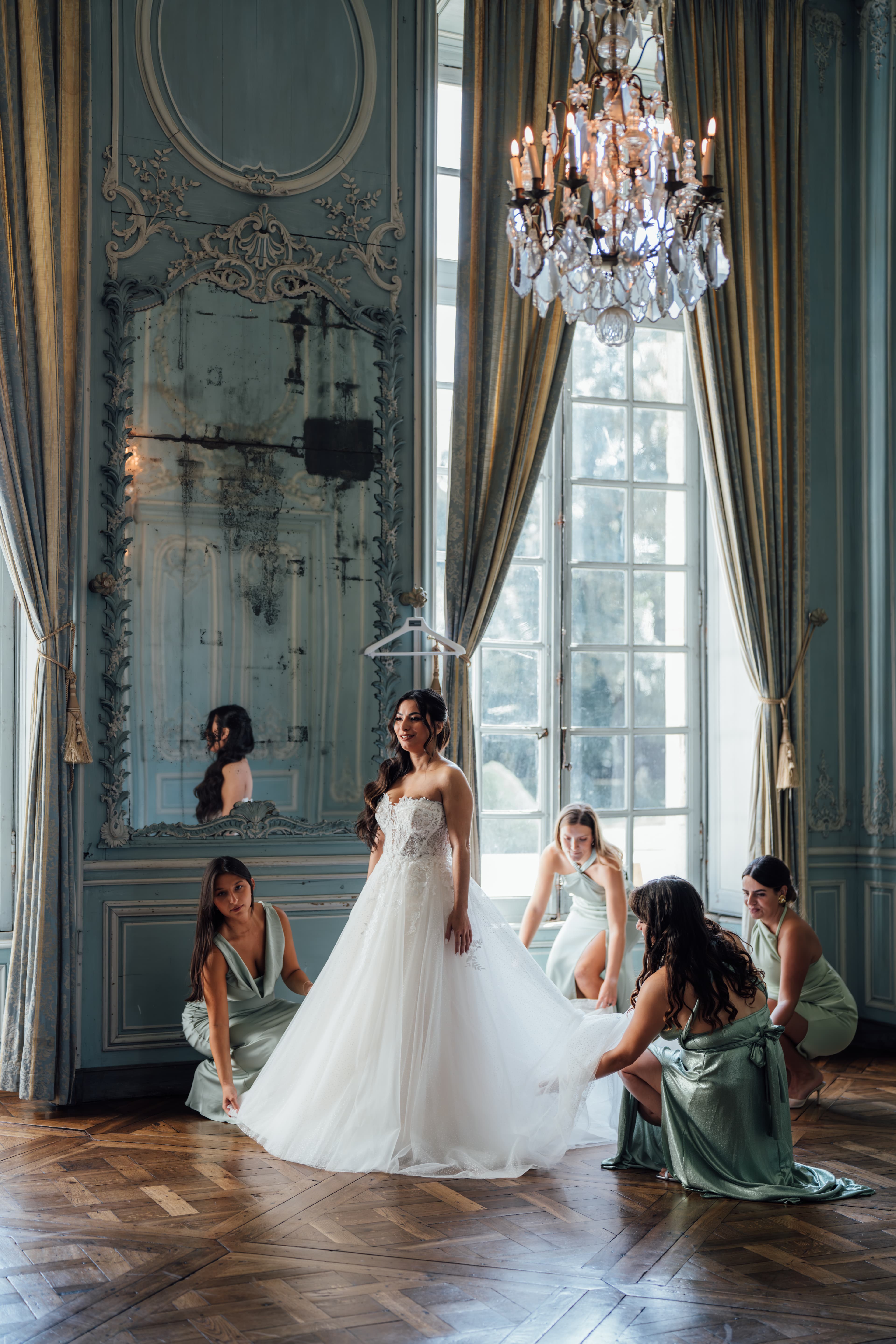 mariée marine et ses demoiselles d'honneur ajustent la robe de la mariée au château de champlatreux