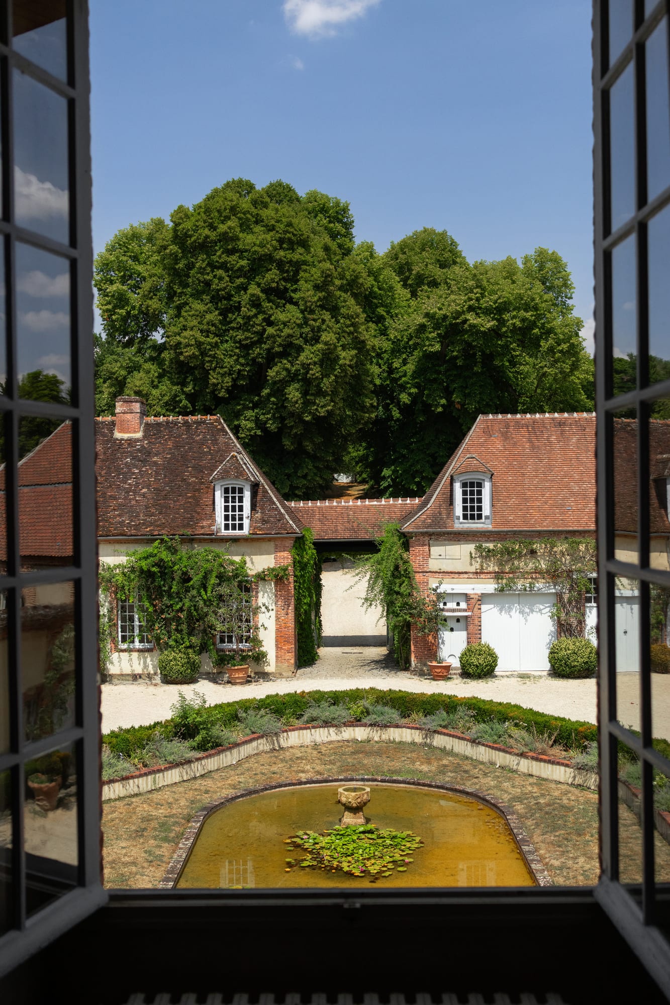 vue depuis une fenêtre sur la cour intérieure et son bassin aux jardins du grand courtoiseau